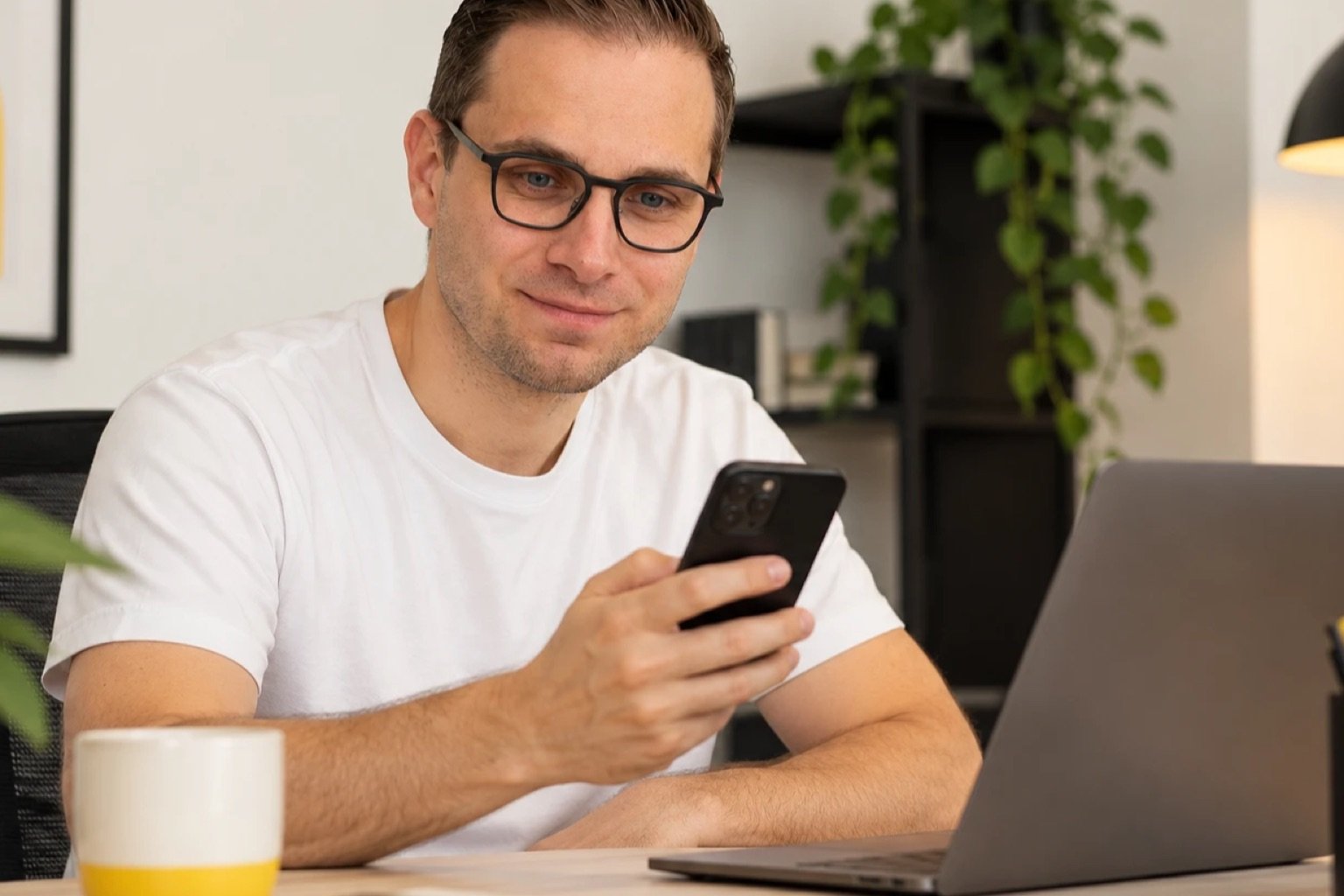 Wesley Eeckhout bekijkt een website op zijn telefoon, met een laptop naast zich.